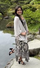RaeAnn Uyeda standing on rock in front of green shrubs in a garden, smiling at camera