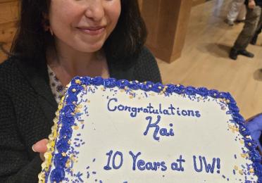 Kai holding a sheet cake that reads "Congratulations, Kai. 10 years at UW!" 